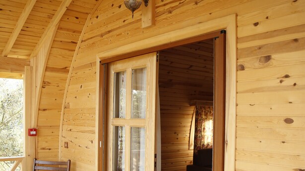 A wooden cabin with a wooden deck, a door leading inside, and two wooden chairs on the deck. - Kazdagları Saglikli Yasam Tatil Koyu (Edremit)