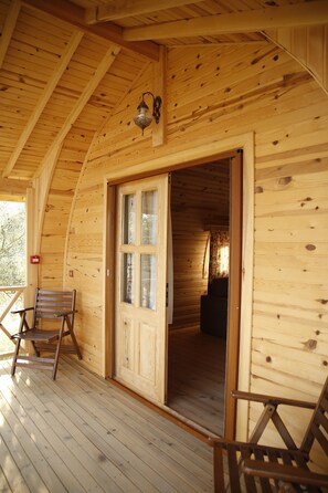 Eine Holzhütte mit einer Holzterrasse, einer Tür zum Eingang und zwei Holzstühlen auf der Terrasse.