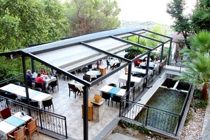 An outdoor dining area with tables and chairs, surrounded by greenery and a small water feature. - Kazdagları Saglikli Yasam Tatil Koyu (Edremit)
