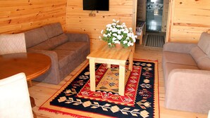 A cozy cabin interior with a wooden interior, a television mounted on the wall, a sofa, a table, and a potted plant. - Kazdagları Saglikli Yasam Tatil Koyu (Edremit)