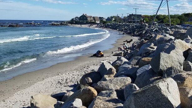Ein felsiger Strand mit Wellen, einem klaren Himmel und weit entfernten Gebäuden.