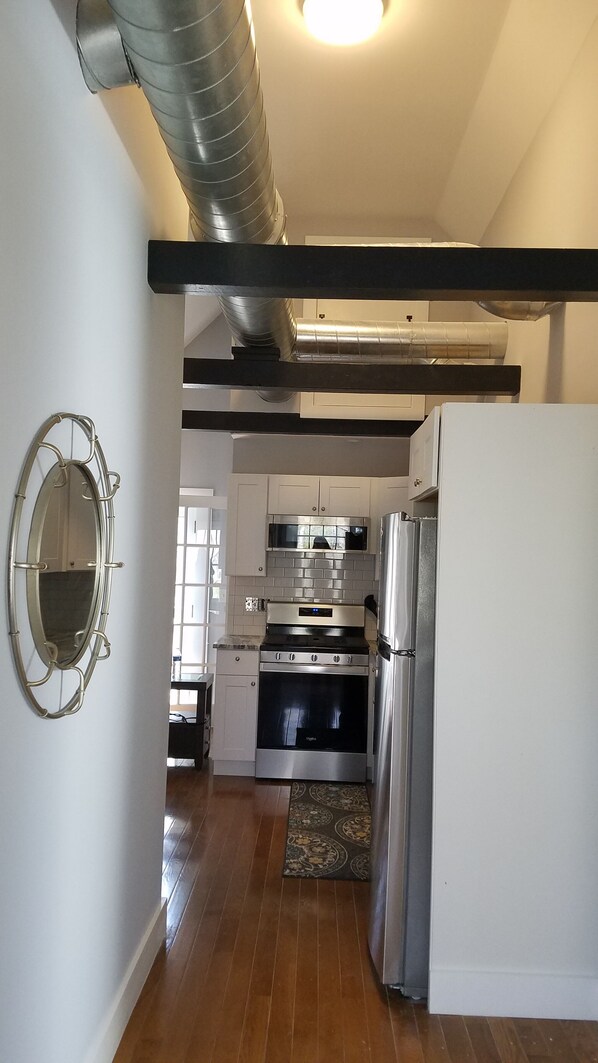 A modern kitchen with stainless steel appliances, a wooden floor, and a large mirror. - Loft Style ,Sleep 4, 2 mins to Beach, UNE, dining, outlets, fishing, EVERYTHING! (Biddeford)