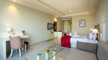 A hotel room with a bed, a desk, a chair, a glass coffee table, and a red throw blanket.