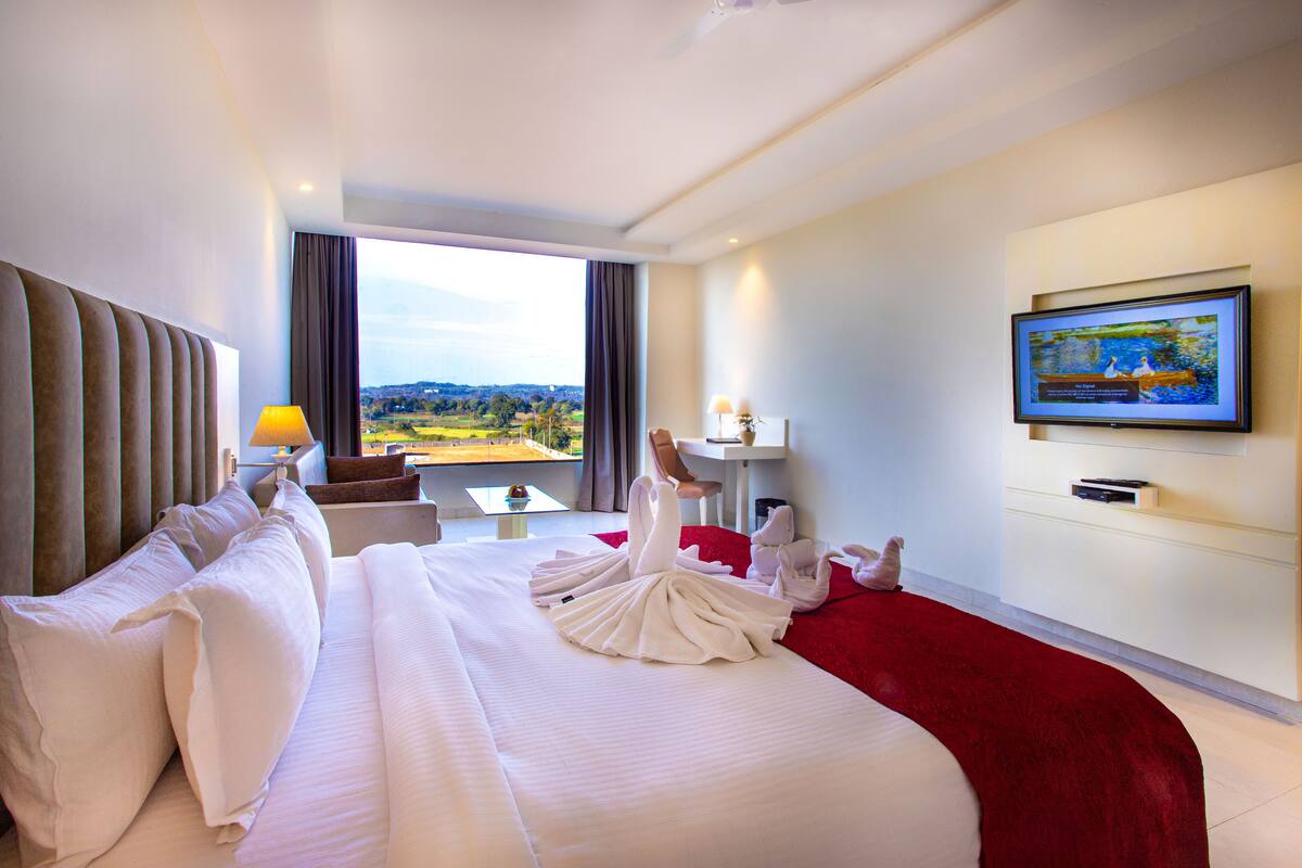 Een hotelkamer met een groot bed, een aan de muur bevestigde televisie en uitzicht op het landschap door het raam.