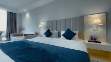 Een moderne hotelkamer met een groot bed, een nachtkastje met lamp, een fauteuil en een bijzettafeltje.