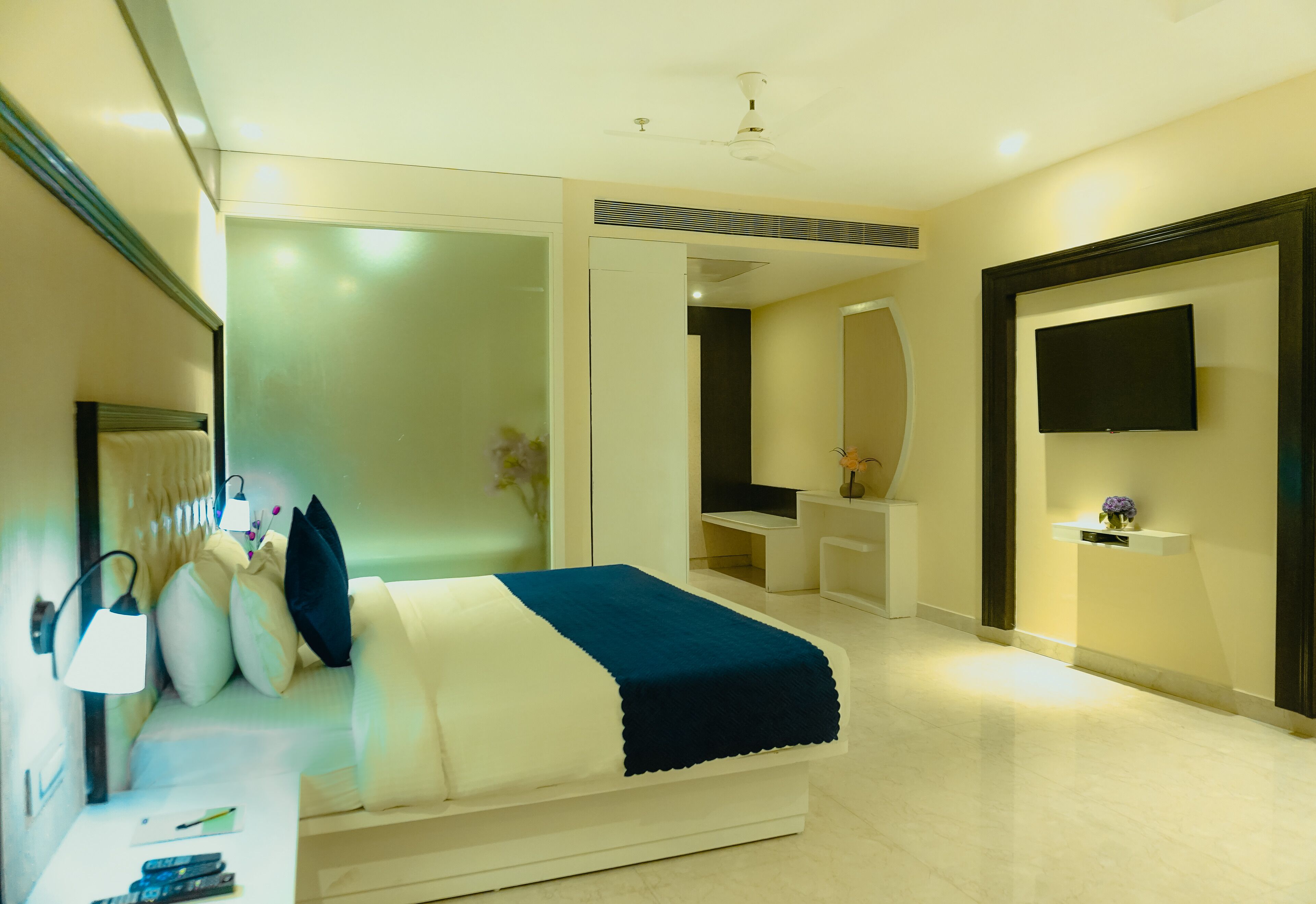 A modern bedroom with a bed, bedside table, lamp, and a TV mounted on the wall.