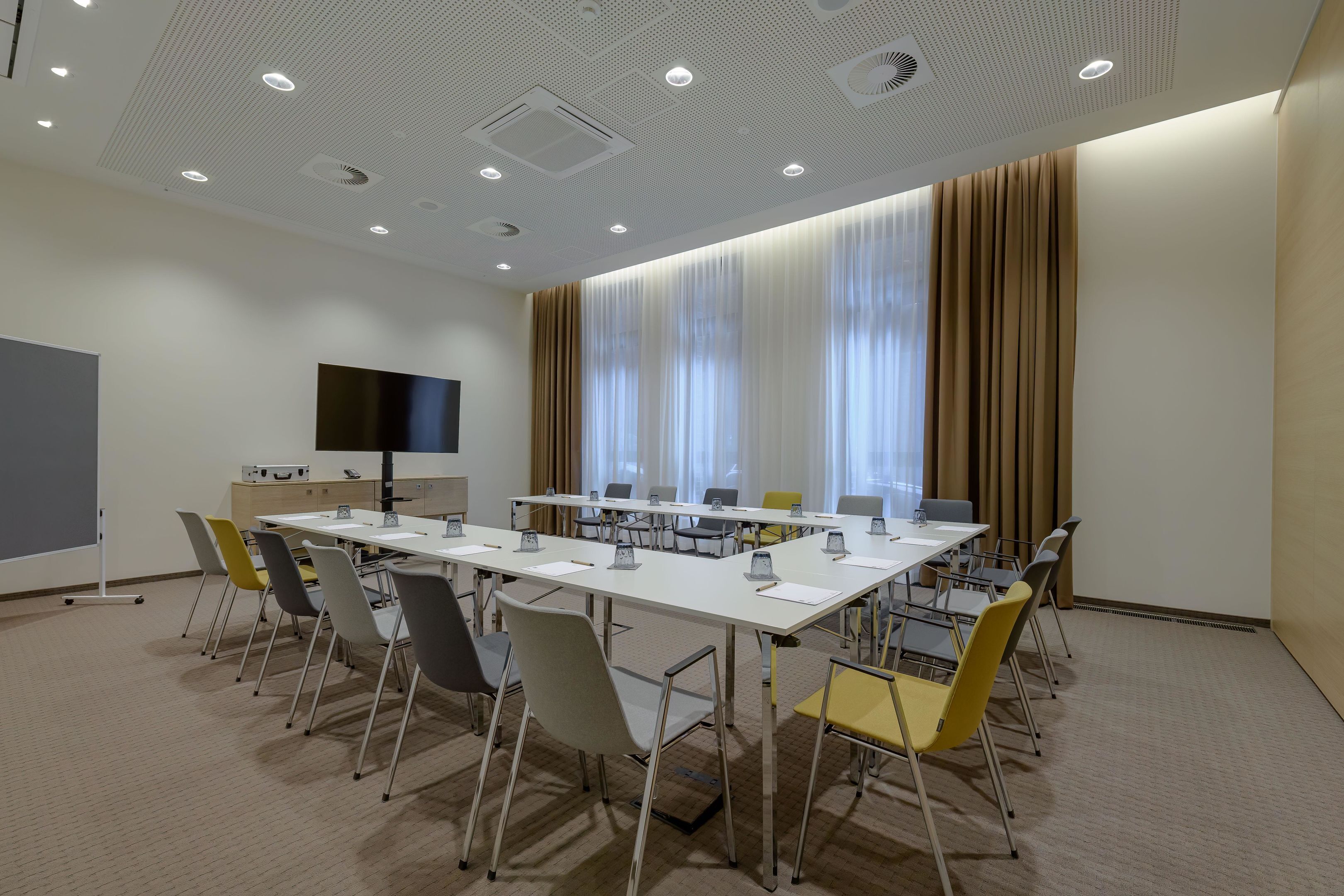 A conference room with a long table, chairs, a flat-screen TV, and a large window with curtains.