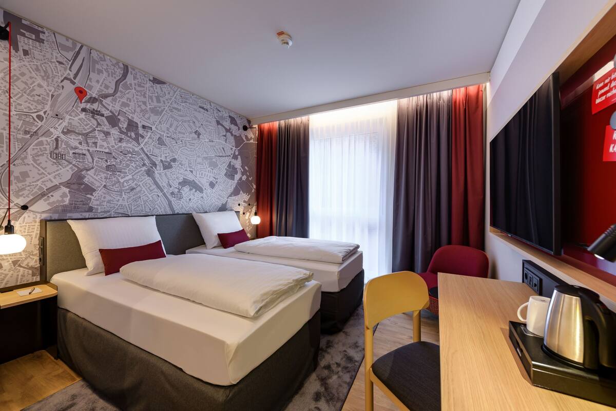 A hotel room with two beds, a desk with a chair, a TV, and a map on the wall.