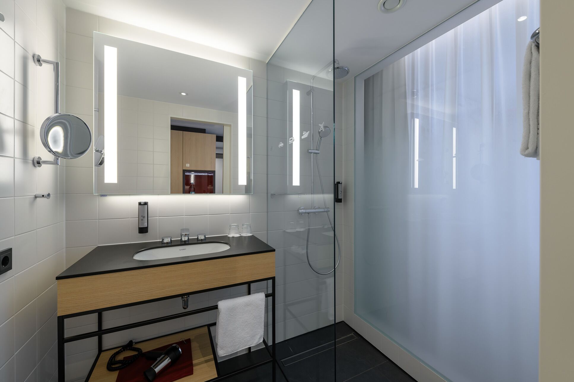A modern bathroom with a glass shower enclosure, a large mirror, and a vanity with a sink and towel rack.