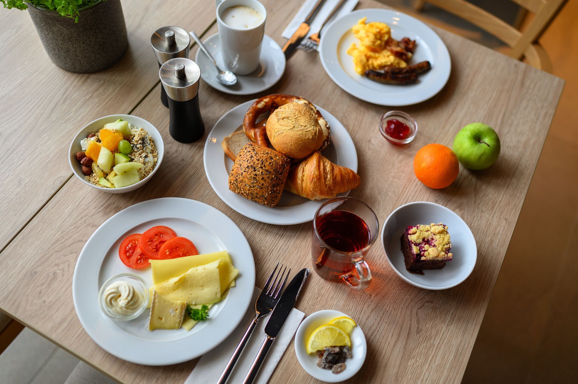 A breakfast setting with various dishes, including croissants, scrambled eggs, and a slice of cake.