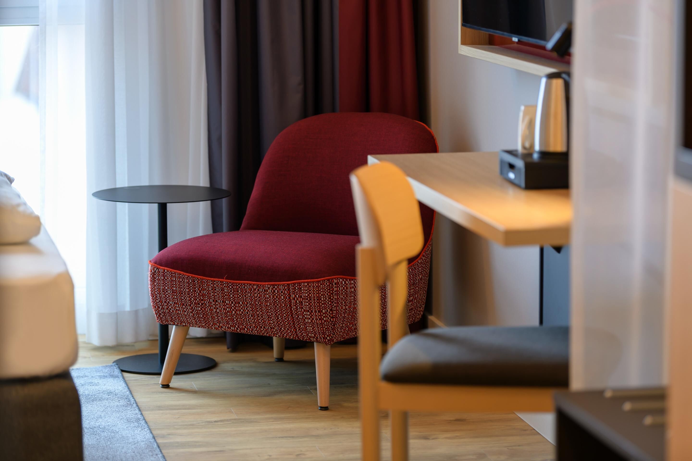 Ein modernes Zimmer mit einem rot gepolsterten Sessel, einem Holztisch und einem kleinen runden Tisch.
