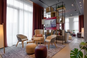 Un salon moderne comprenant un canapé, des fauteuils, un pouf et un téléviseur fixé au mur.