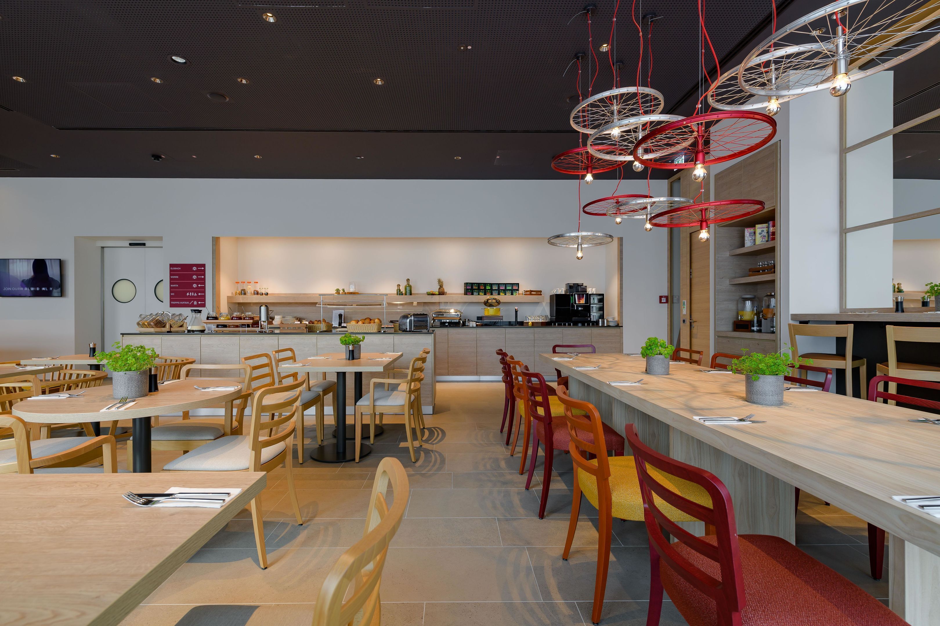 Ein modernes Restaurant mit mehreren Essbereichen, darunter ein langer Gemeinschaftstisch und einige kleinere Tische.