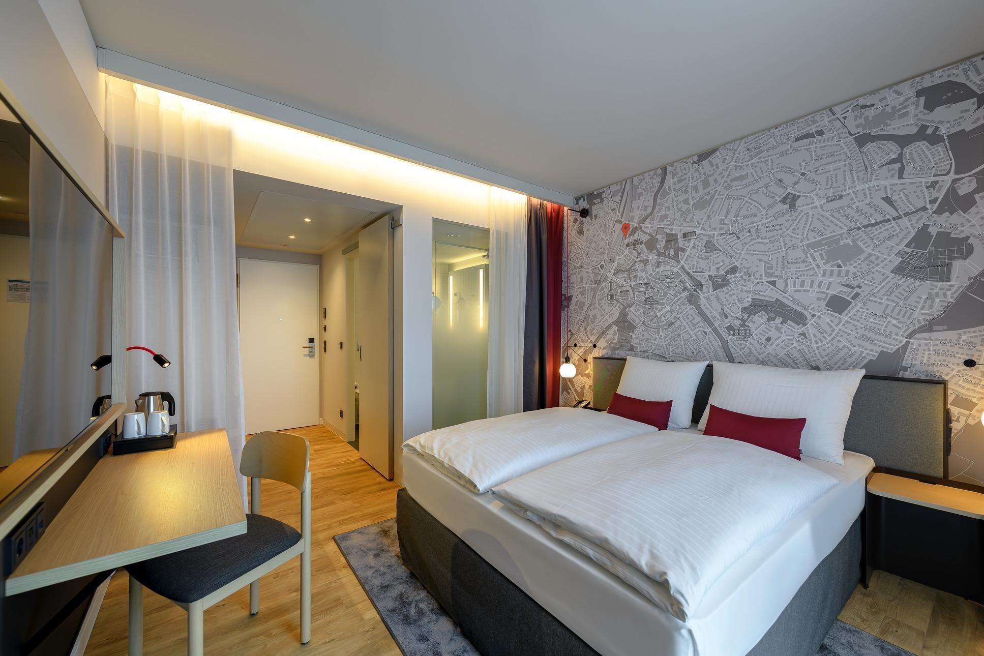 Ein modernes Hotelzimmer mit einem großen Bett, einem Schreibtisch mit Stuhl, einer Karte an der Wand und einem separaten Badezimmerbereich.