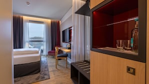 Een moderne hotelkamer met een bed, een bureau, een stoel, een televisie en een minibar.