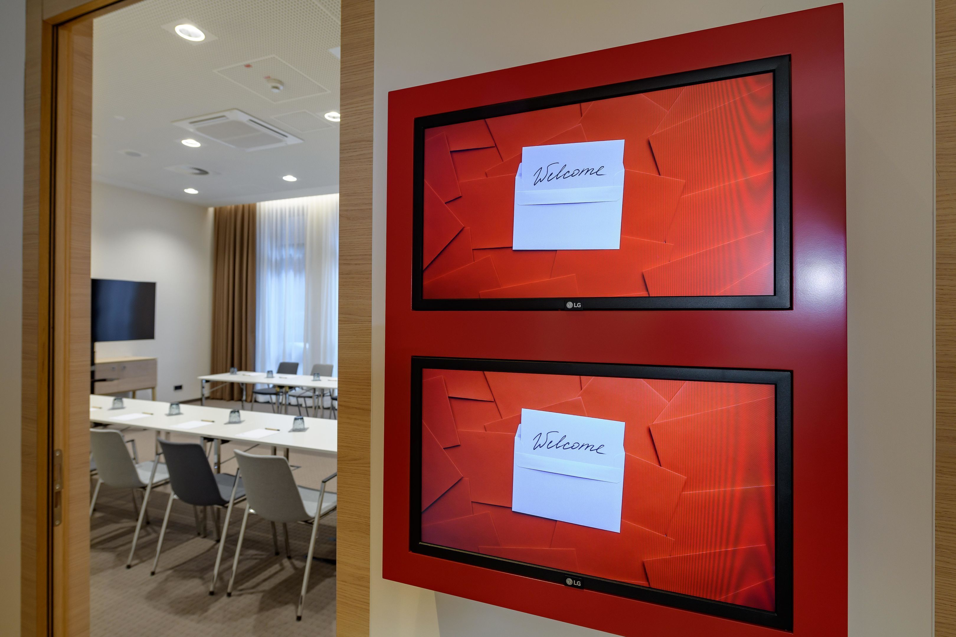 Une salle de conférence équipée de deux écrans LG affichant des messages d’accueil, d’une longue table avec des chaises et d’un téléviseur placé à gauche.