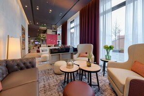 Un hall d’hôtel moderne avec un espace salon, une table basse et une bibliothèque.