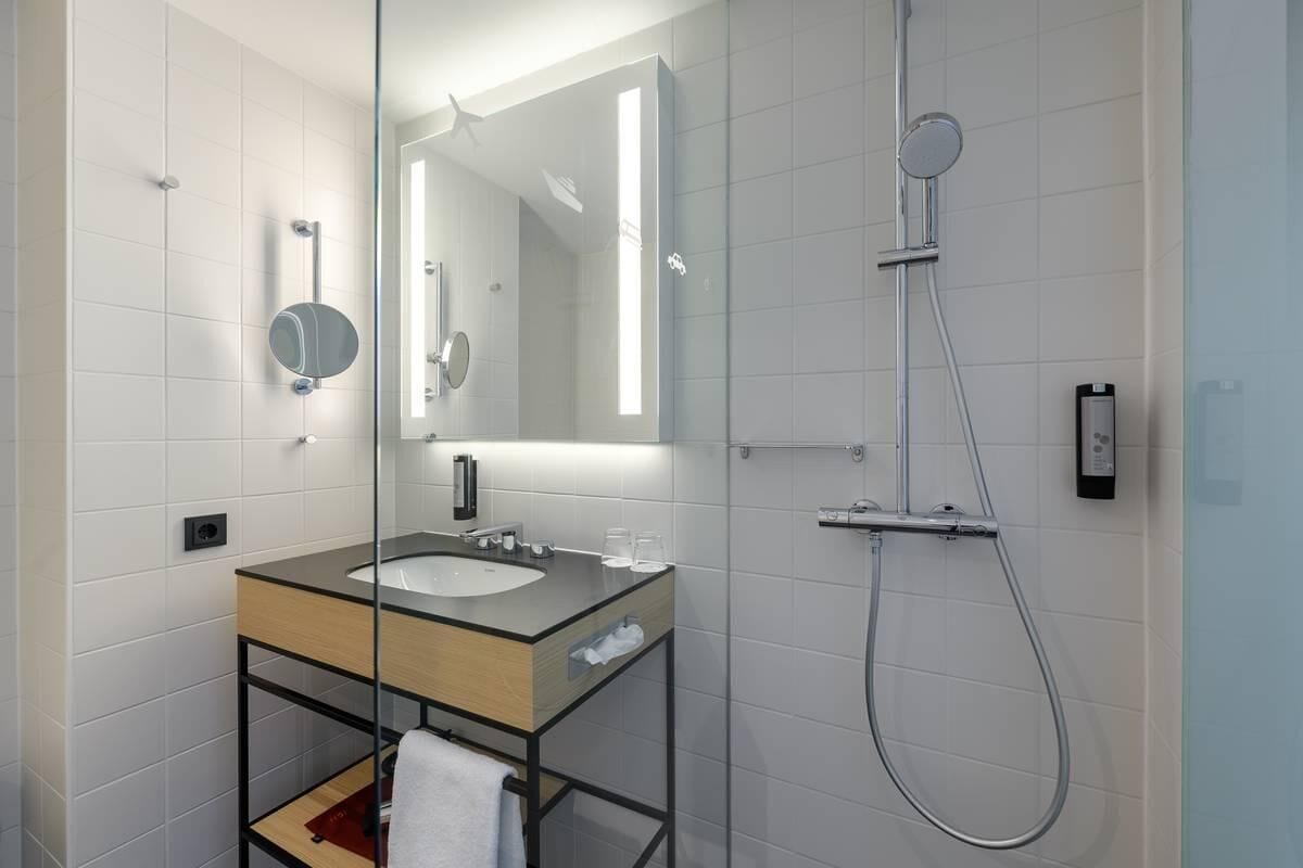 Un baño moderno con ducha acristalada, tocador de madera y un espejo grande.