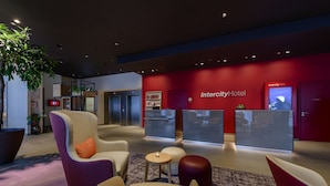 Een moderne lobby met zitplaatsen, een receptiebalie en een rode muur met de naam Intercity Hotel.