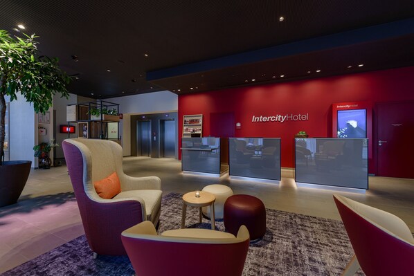 Un vestíbulo moderno con asientos, un mostrador de recepción y una pared roja con el nombre Intercity Hotel.
