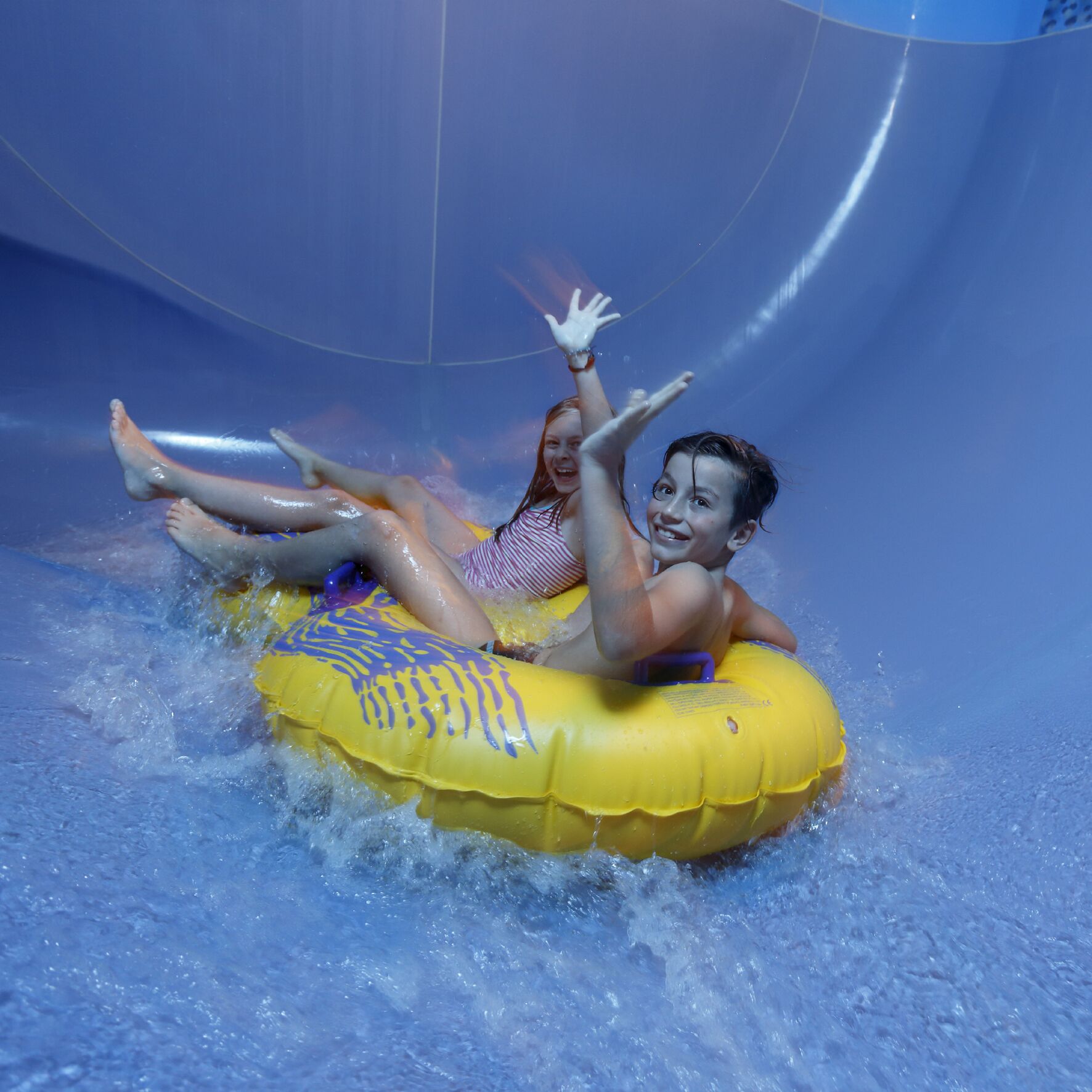 Zwei Personen auf einem gelben Luftschlauch in einer Wasserrutsche.