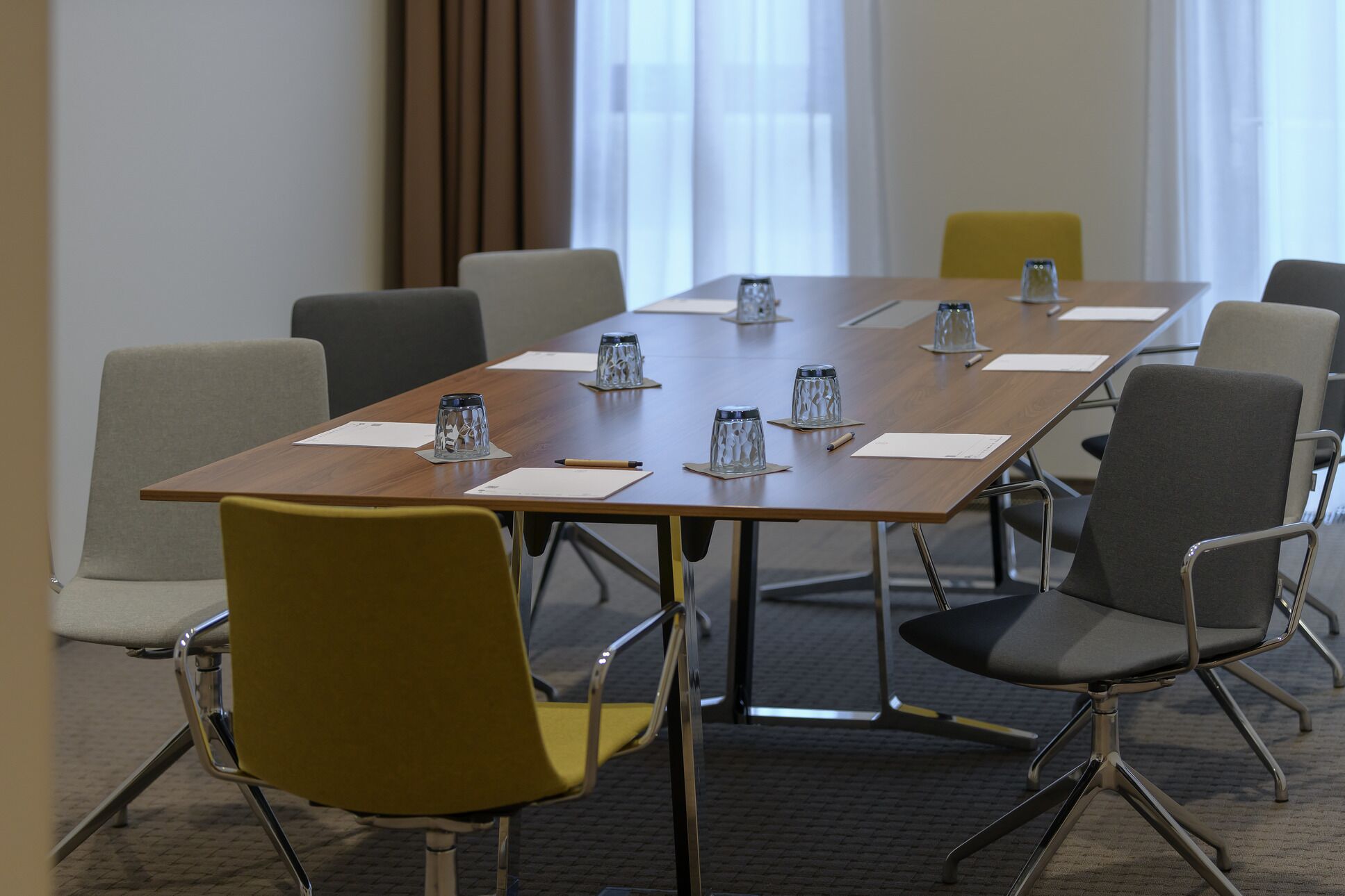 Un salón de conferencias con una larga mesa, múltiples sillas y jarrones de vidrio con agua en cada asiento.