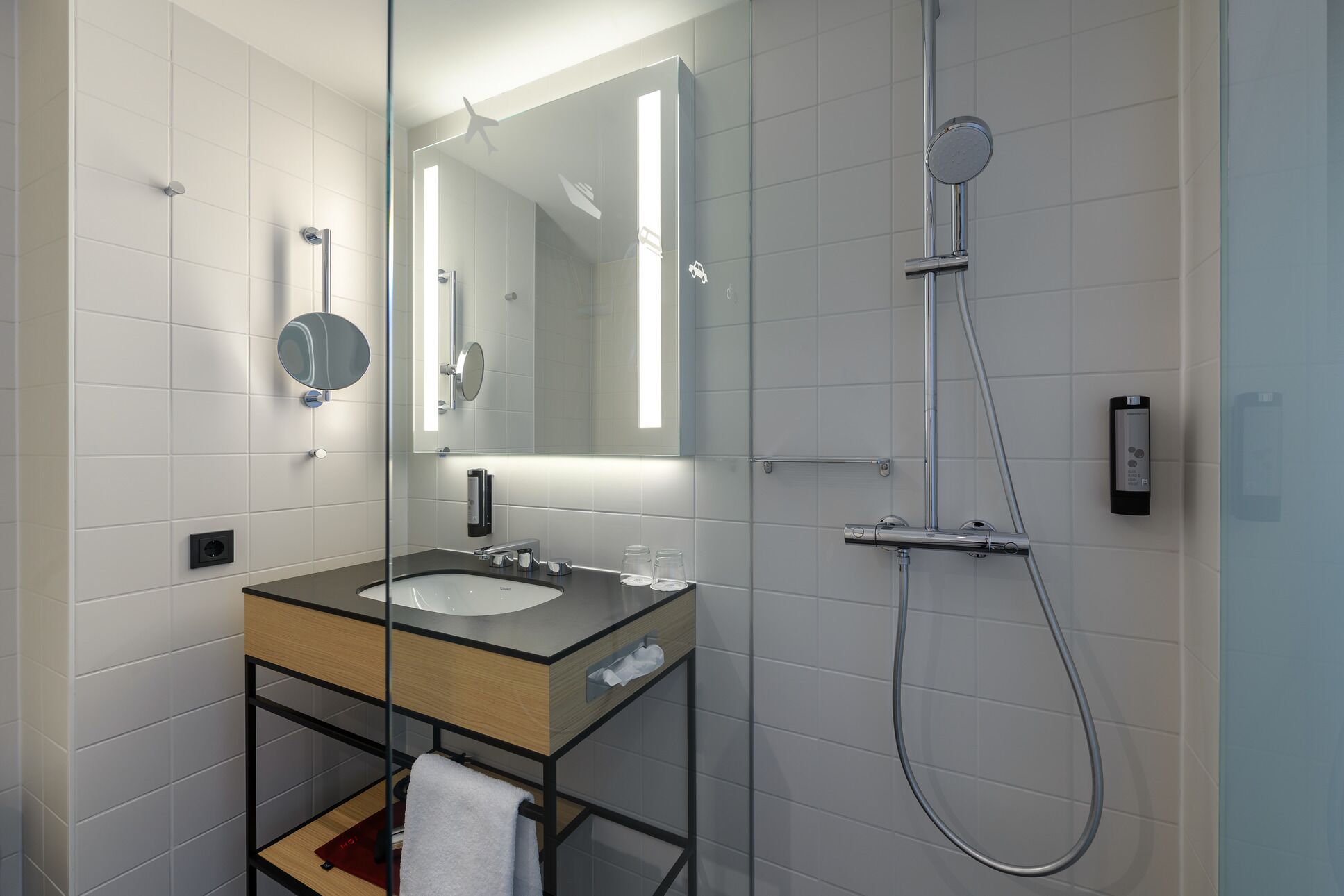Un baño moderno con cabina de ducha de vidrio, un lavamanos con espejo y un perchero para toallas.