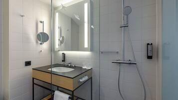Un baño moderno con cabina de ducha de vidrio, un lavamanos con espejo y un perchero para toallas.
