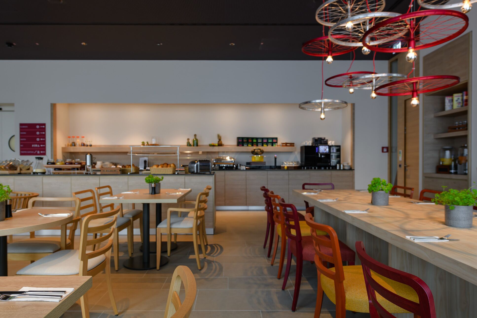 Ein modernes Restaurant mit Holztischen und -stühlen, einer Bar und roten Pendelleuchten.