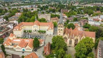 An aerial view of a town with a prominent church, a large building with a red roof, and surrounding greenery.