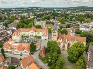 Eine Vogelperspektive einer Stadt mit einer markanten Kirche, einem großen Gebäude mit rotem Dach und umgebender Grünfläche.