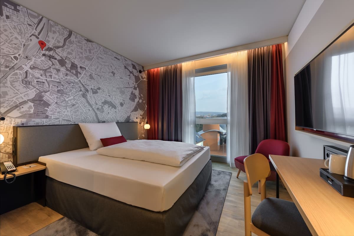 A hotel room with a large bed, a desk, a chair, a TV, and a map on the wall.