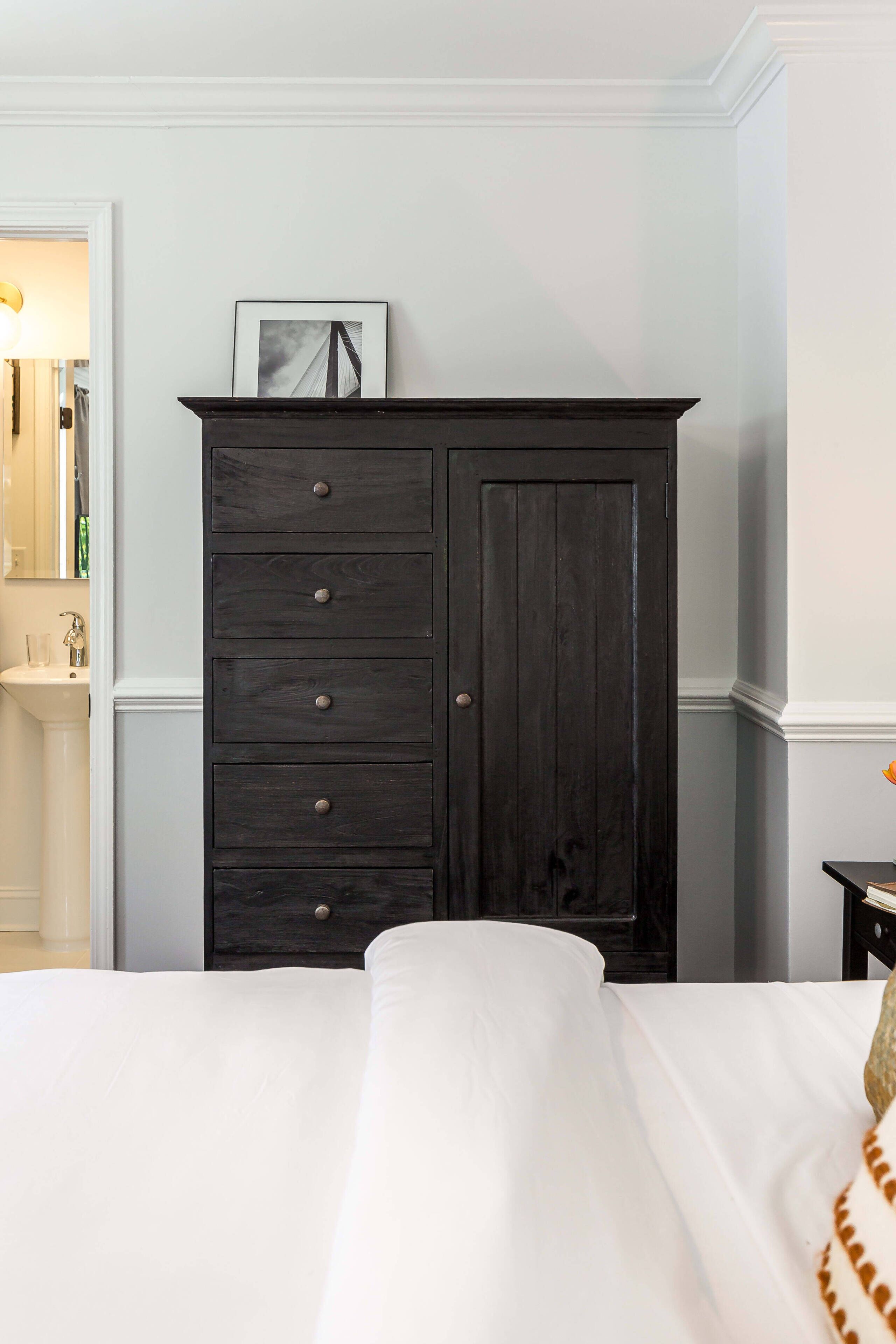 Een slaapkamer met een donkere houten dressoir, een wit bed en een klein tafeltje met een lamp.