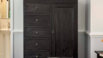 Een slaapkamer met een donkere houten dressoir, een wit bed en een klein tafeltje met een lamp.