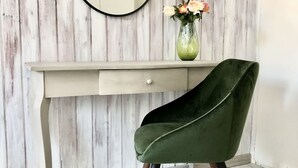 Un escritorio con espejo, una silla verde y un florero con flores frente a una pared de madera.
