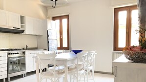 Una cocina moderna con armarios blancos, una estufa a gas y un comedor con sillas blancas y un tazón azul.