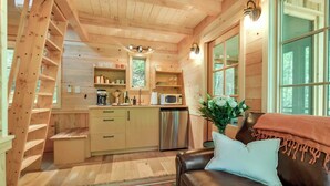 A cozy cabin interior with a wooden interior, a kitchenette, a dining area, and a living room with a sofa and a decorative vase. - Maple Treehouse | Unique, Private, Romantic (Gatlinburg)