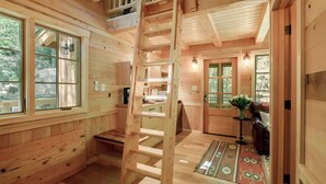 A wooden cabin interior with a loft bedroom, a kitchen area, and a living space with a view of the outdoors. - Maple Treehouse | Unique, Private, Romantic (Gatlinburg)