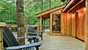 Una terraza de madera con sillas Adirondack y un ventanal que da a una cabaña.
