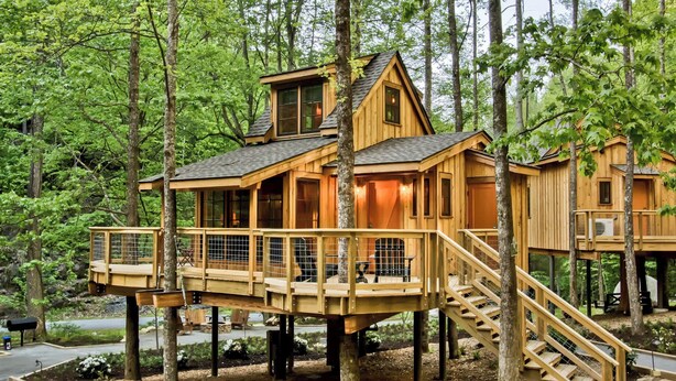 Una casa del árbol de madera con balcón y escalera, rodeada de un bosque.