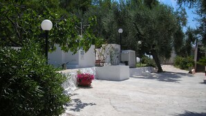 Une cour avec un mur blanc, un jardinier avec des fleurs roses et un lampadaire.