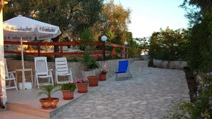 Un espace extérieur aménagé avec un sol en pierre, des chaises blanches et bleues, et des plantes en pot.