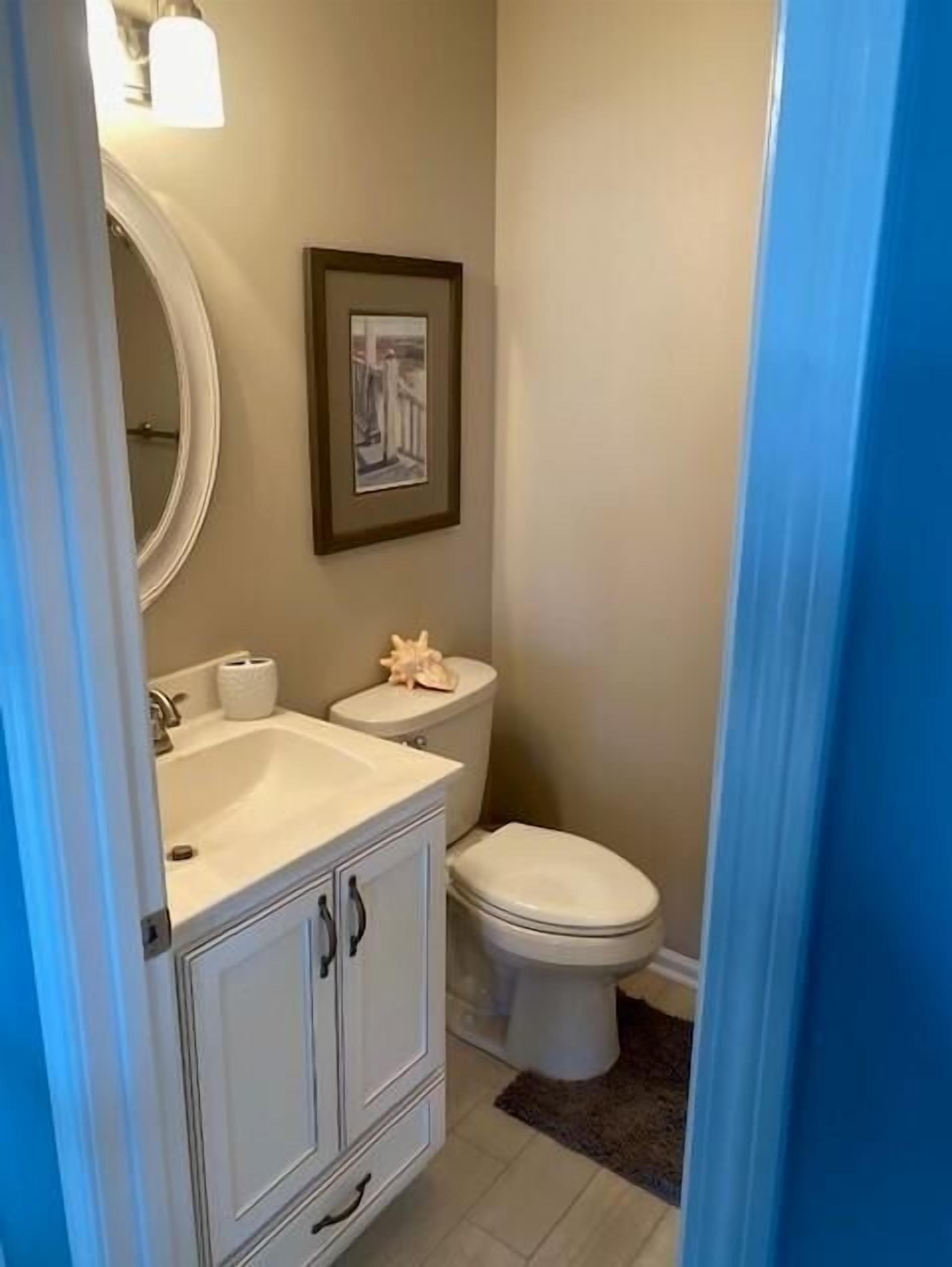 A bathroom with a white sink, toilet, and vanity. There is a framed picture on the wall above the toilet.