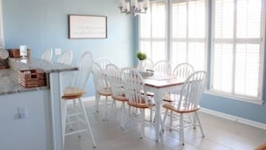 A dining area with a light blue wall, white chairs, a wooden table, and a chandelier.