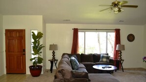 Sala de estar con sofá, reposapiés, dos lámparas, planta en maceta y ventilador de techo.