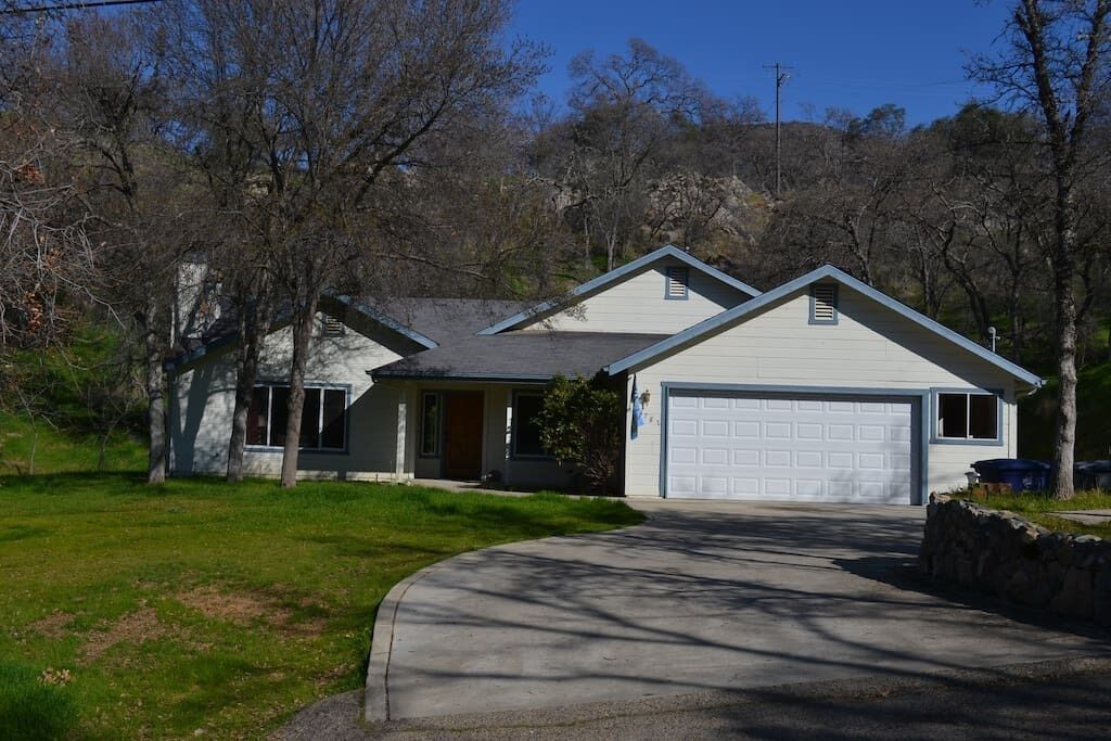 A single-story house with a garage, surrounded by trees and a grassy yard.