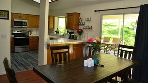 Una cocina moderna con armarios de madera, un microondas integrado y un horno. Cuenta con una zona de comedor con mesa y sillas, y vistas al exterior a través de amplios ventanales.