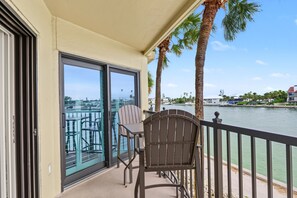 A balcony with a view of a marina, a table, and two chairs.