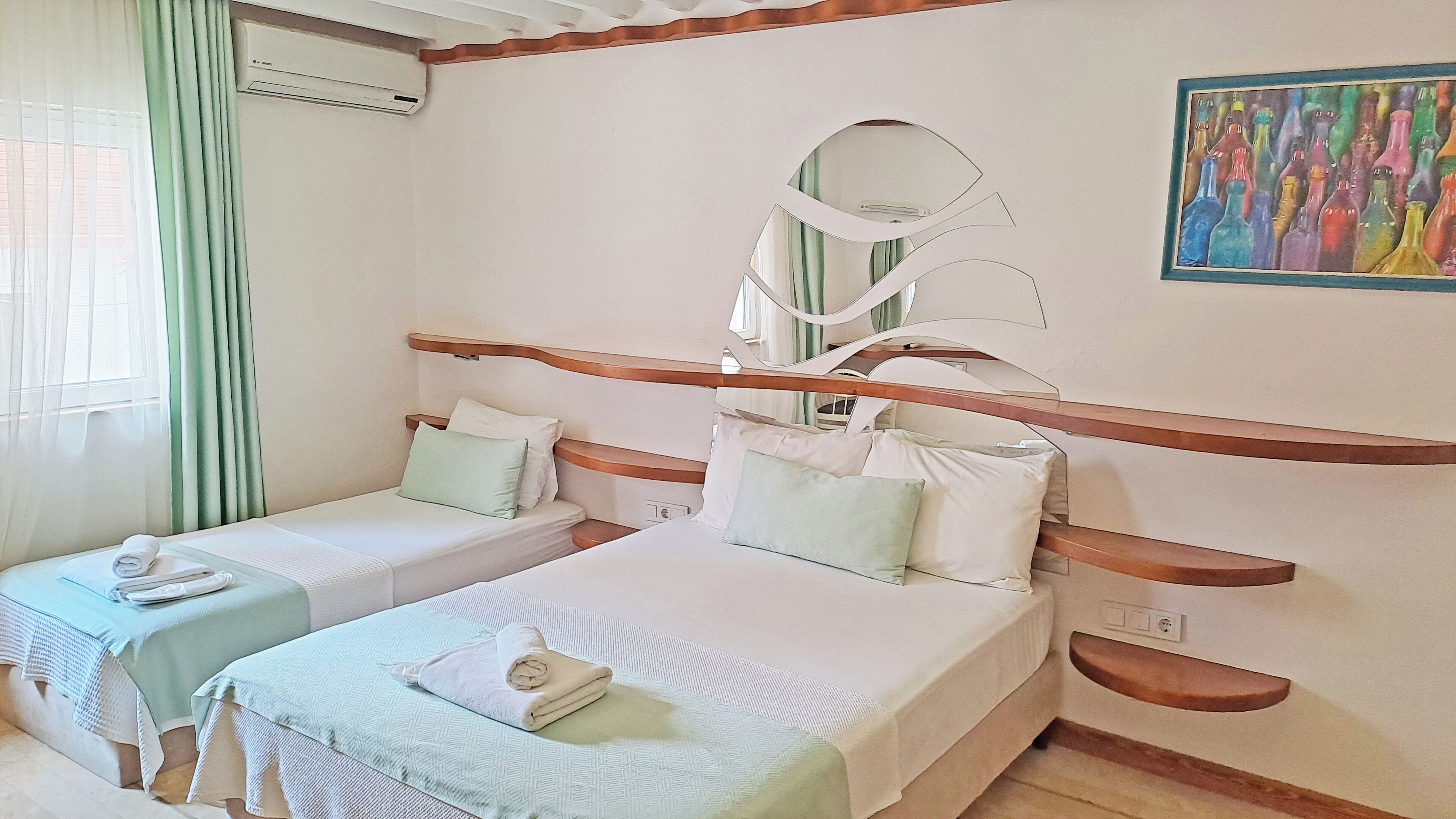 A hotel room with two single beds, a large mirror, and a painting on the wall.
