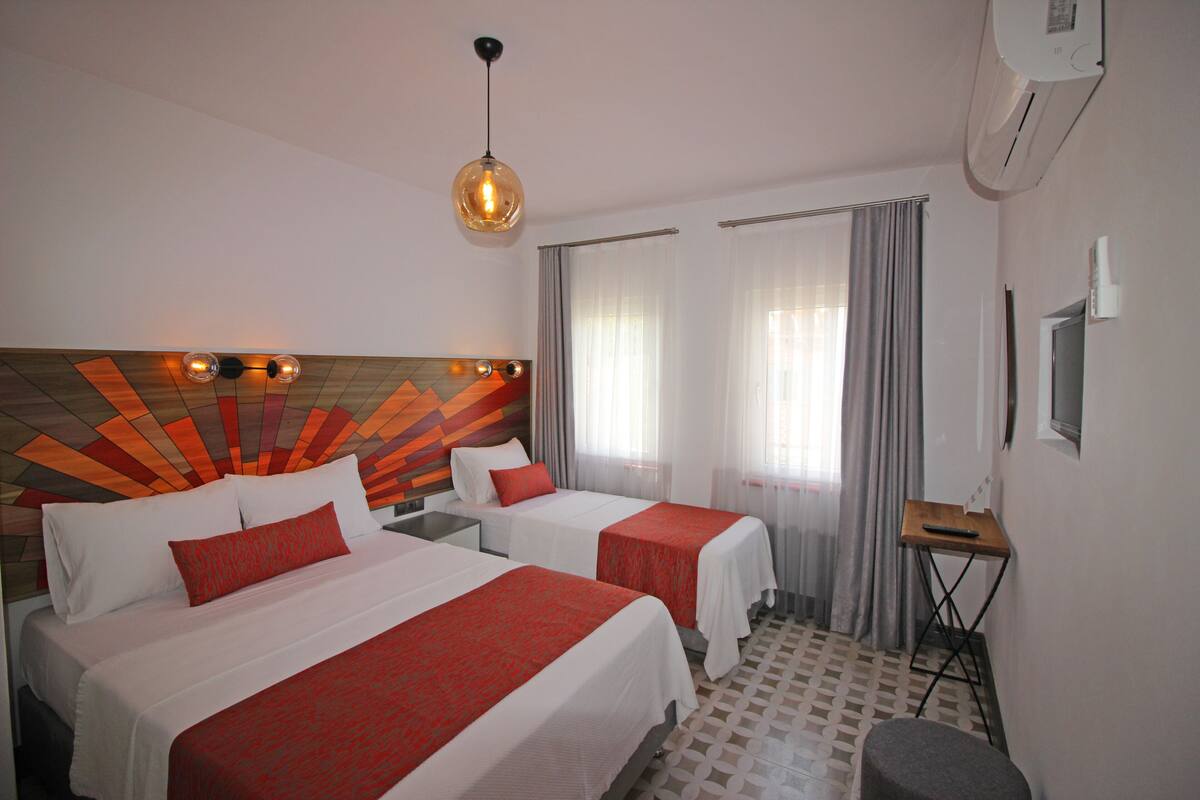 A hotel room with two beds, a wooden headboard, a desk, a chair, and a ceiling fan.